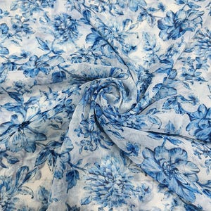 Könnte beinhalten: Nahaufnahme eines weißen Stoffes mit blauem Blumenmuster. Das Design zeigt große, detaillierte blaue Blumen und Blätter, die eine zarte und elegante Ästhetik schaffen. Der Stoff ist leicht zerknittert und verleiht dem Gesamtbild Textur.