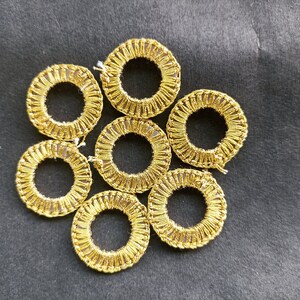 May include: Seven gold-colored circular embellishments with a hole in the center, arranged in a flower-like pattern on a black background.