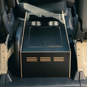 May include: A custom black and woodgrain center console with two cup holders, a storage compartment, and the text "ROUTED WILD". The console has a honeycomb pattern and three horizontal vents.