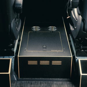 May include: Black and gold interior console with two cup holders and a storage compartment. The console has a textured surface and gold trim. The text "ROUTED WILD" is visible on the top.