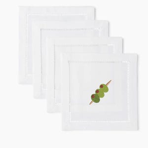 Peut inclure: Quatre serviettes de cocktail carrées blanches avec une bordure cousue. Une serviette présente un motif brodé de trois olives vertes sur une brochette en bois. Les serviettes sont en tissu blanc doux.