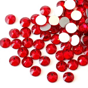 May include: A large quantity of small, red, round rhinestones. The rhinestones are scattered on a white surface.