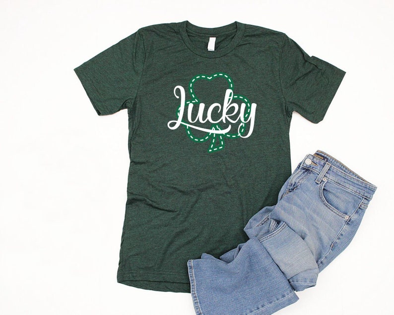 May include: A dark green t-shirt with a white graphic of a shamrock and the word "lucky" in a white cursive font.