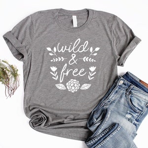 Op de afbeelding: Grijs T-shirt met witte tekst die "wild & free" zegt met bloemmotieven.