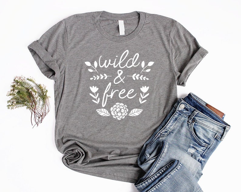Op de afbeelding: Grijs T-shirt met witte tekst die "wild & free" zegt met bloemmotieven.