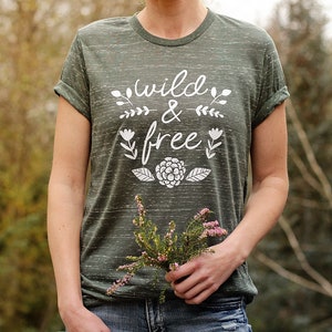 Op de afbeelding: Een groen T-shirt met een witte afbeelding die "wild & free" zegt met bloemmotieven.