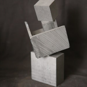 May include: A gray geometric sculpture made of stacked rectangular blocks. The blocks are arranged in a unique and abstract way, creating a visually interesting piece.