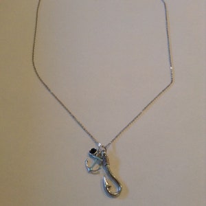 May include: Silver-toned necklace featuring a fishing hook and anchor pendant. The hook is detailed with wrapped wire, and the anchor has a small black accent. The chain is delicate, and the clasp is visible at the top.