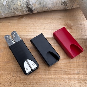 May include: Two black cases for a multi-tool, one with a silver multi-tool inside, and one red case.