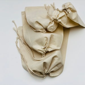 May include: A stack of four natural cotton drawstring bags. The bags are made of a soft, natural fabric and have a simple, rustic look.
