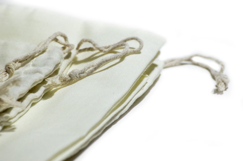 May include: A white cotton drawstring bag with a natural cotton cord. The bag is folded and the cord is tied in a knot.