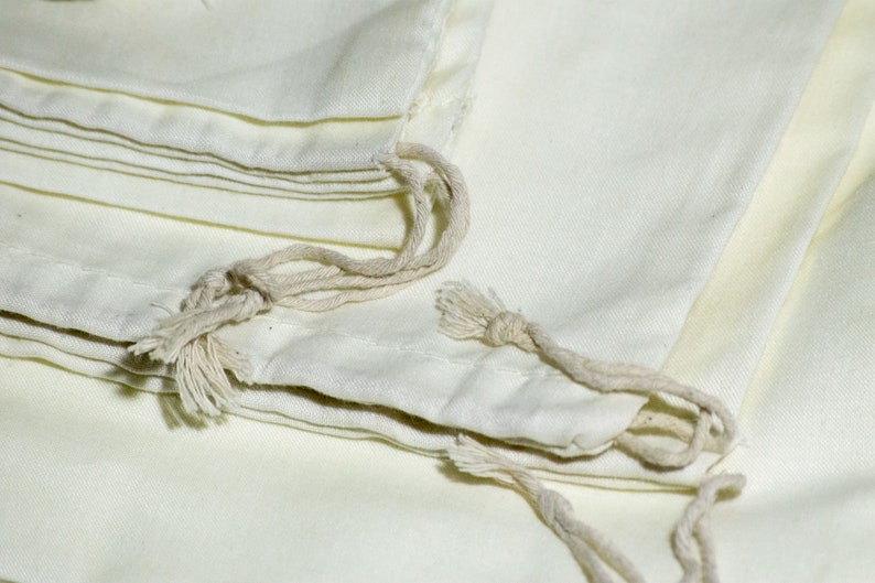 May include: A stack of white cotton drawstring bags with natural cotton drawstrings. The bags are folded and stacked on top of each other.
