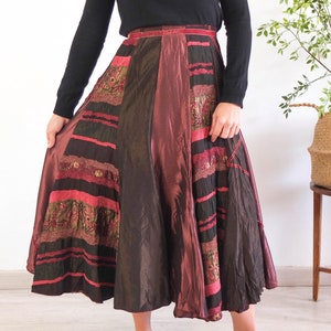 Può includere: Una lunga gonna multicolore con un design a patchwork. La gonna è realizzata con diversi tessuti e texture, tra cui seta, velluto e pizzo. La gonna è un mix vibrante di colori rosso, marrone e oro.