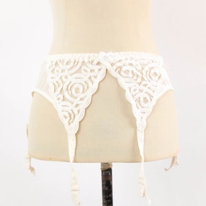 May include: White lace suspender belt with four straps. The suspender belt is made of delicate white lace with a floral pattern.