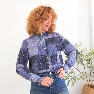 May include: A blue and white patterned long-sleeved shirt with a button-up collar. The shirt has a patchwork design with different shades of blue and white.