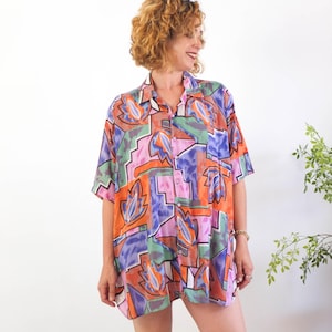 May include: A patterned button-down shirt in a variety of colours, including orange, pink, purple, green, and blue. The short-sleeved shirt has a collared neckline and a loose fit. The shirt is ideal for a casual look.