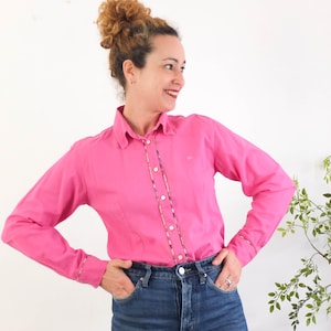 May include: A pink long-sleeved button-down shirt with a white collar and a multi-coloured stripe down the front. The shirt has a small embroidered logo on the left chest.