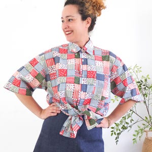 Può includere: Una camicia patchwork con quadrati rossi, blu, verdi e bianchi, annodata in vita. La camicia ha maniche corte e un colletto. La persona indossa una gonna di jeans blu scuro.