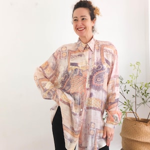 Può includere: Camicia a maniche lunghe con motivo paisley e geometrico nei toni del pesca, lavanda e oro. La camicia ha un colletto e una vestibilità ampia, adatta all'abbigliamento casual. Il tessuto appare leggero e semitrasparente.