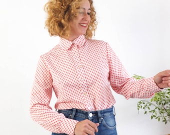 May include: A button-down shirt with a repeating red diamond pattern on a white background. The long-sleeved shirt is paired with blue jeans. The collar is buttoned up, and the sleeves are buttoned at the cuffs.