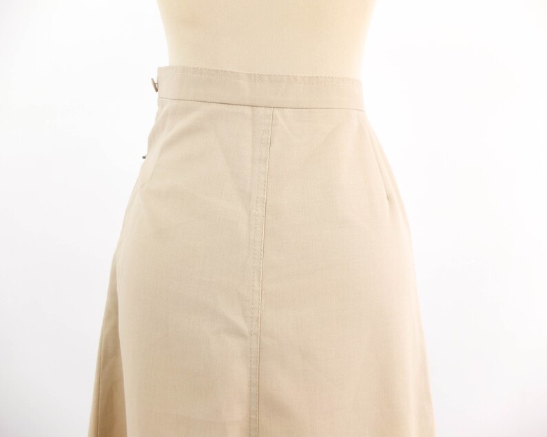 May include: A beige skirt with a straight cut and a simple design. The skirt is made of a lightweight fabric and has a zip closure at the back.