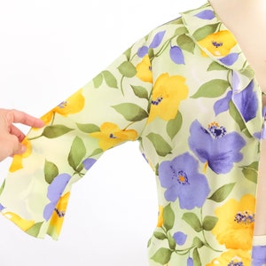 May include: A light green, yellow, and purple floral print blouse with a ruffled collar and a tie at the neck.