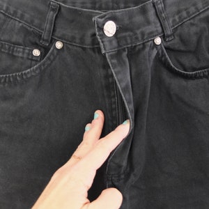 May include: Black denim jeans with a zipper fly and a button closure. The jeans have a classic five-pocket style.