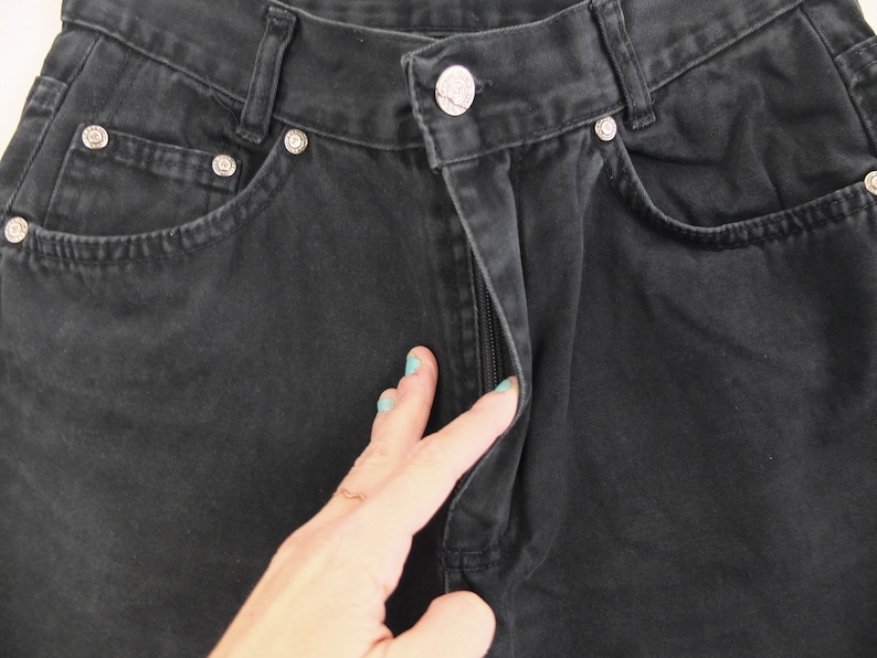 May include: Black denim jeans with a zipper fly and a button closure. The jeans have a classic five-pocket style.