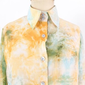 Op de afbeelding: Een overhemd met een tie-dye patroon in tinten geel, oranje en groen. De kraag en manchetten zijn een lichtere tint geel en blauw. Het overhemd heeft een klassieke kraag en een knoopsluiting.