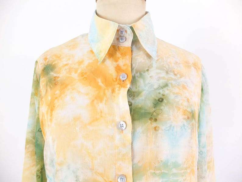 Op de afbeelding: Een overhemd met een tie-dye patroon in tinten geel, oranje en groen. De kraag en manchetten zijn een lichtere tint geel en blauw. Het overhemd heeft een klassieke kraag en een knoopsluiting.