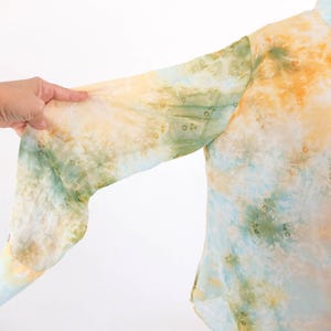 Op de afbeelding: Een overhemd met knoopsluiting en een tie-dye patroon in tinten geel, groen en blauw. De lange mouwen zijn zichtbaar en de stof lijkt licht. Het overhemd heeft een klassieke kraag en knopen.