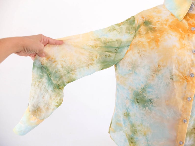 Op de afbeelding: Een overhemd met knoopsluiting en een tie-dye patroon in tinten geel, groen en blauw. De lange mouwen zijn zichtbaar en de stof lijkt licht. Het overhemd heeft een klassieke kraag en knopen.