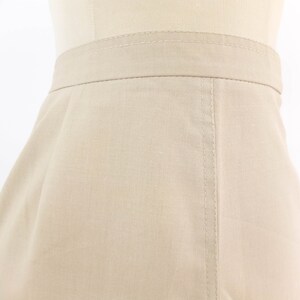 May include: A beige skirt with a straight cut and a seam down the centre back.