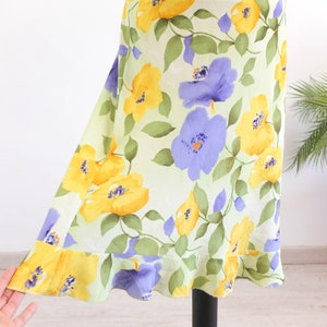 May include: A light green skirt with a floral print featuring yellow and purple flowers. The skirt has a ruffled hem.