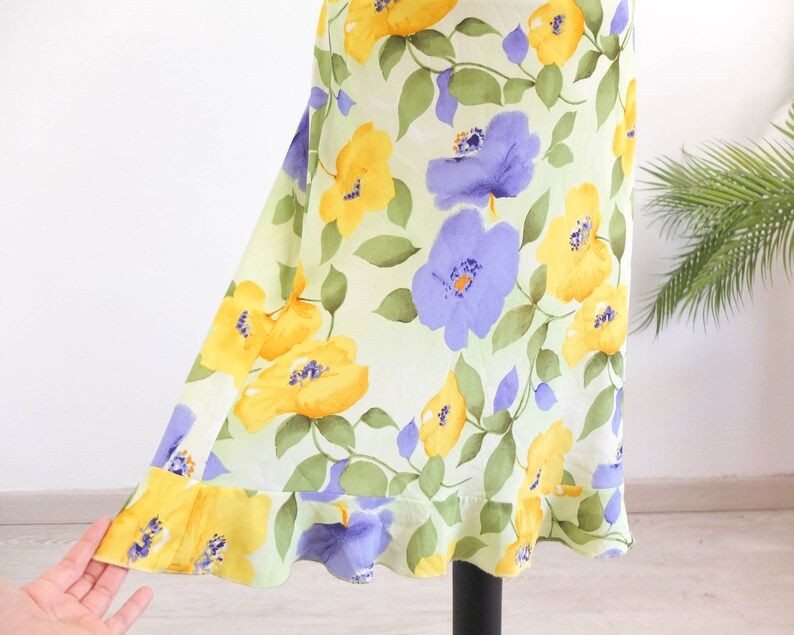 May include: A light green skirt with a floral print featuring yellow and purple flowers. The skirt has a ruffled hem.