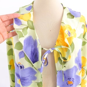 May include: A light green, yellow, and purple floral print blouse with a tie at the front.