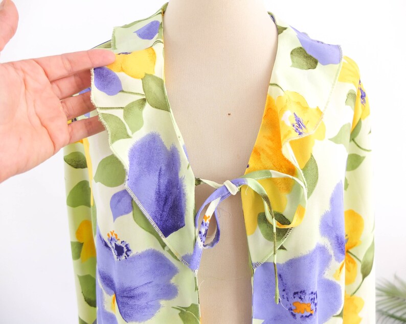 May include: A light green, yellow, and purple floral print blouse with a tie at the front.