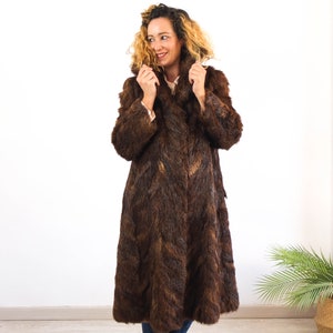 May include: A long brown faux fur coat with a collar. The coat is worn by a person with curly blonde hair.