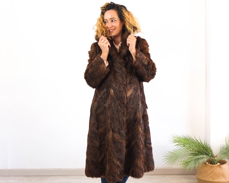 May include: A long brown faux fur coat with a collar. The coat is worn by a person with curly blonde hair.
