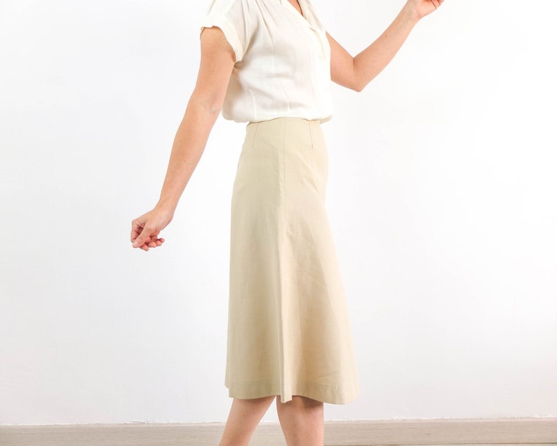 May include: A woman wearing a white blouse and a beige skirt. The skirt is knee-length and has a slight A-line shape.