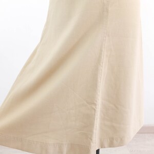 May include: A beige skirt with a straight cut and a slight flare at the bottom. The skirt has a seam down the back and a hemmed edge.