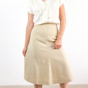 May include: A beige skirt with a straight, A-line silhouette. The skirt is knee-length and has a simple design.
