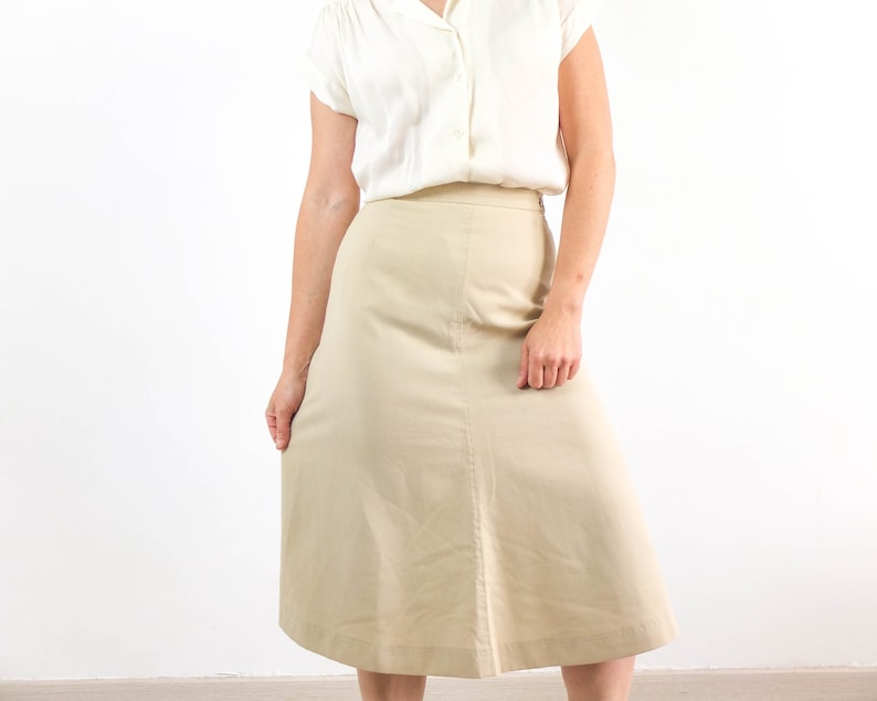 May include: A beige skirt with a straight, A-line silhouette. The skirt is knee-length and has a simple design.