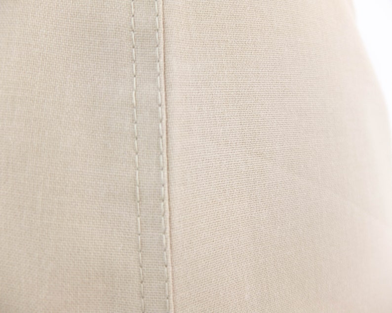 May include: Close-up of a beige fabric with a single seam running down the centre. The fabric has a subtle texture and a slightly off-white colour.