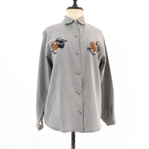 May include: A gray and white checkered button-up shirt with long sleeves and a collared neckline. The shirt features embroidered brown luggage with the text "Long Travel" on the left and right sides.