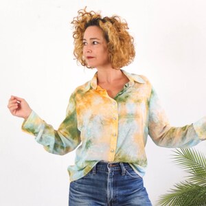 Op de afbeelding: Een overhemd met lange mouwen met een tie-dye patroon in geel, groen en blauw. Het overhemd is geknoopt en wordt gedragen met een blauwe spijkerbroek. Het model staat voor een witte achtergrond.