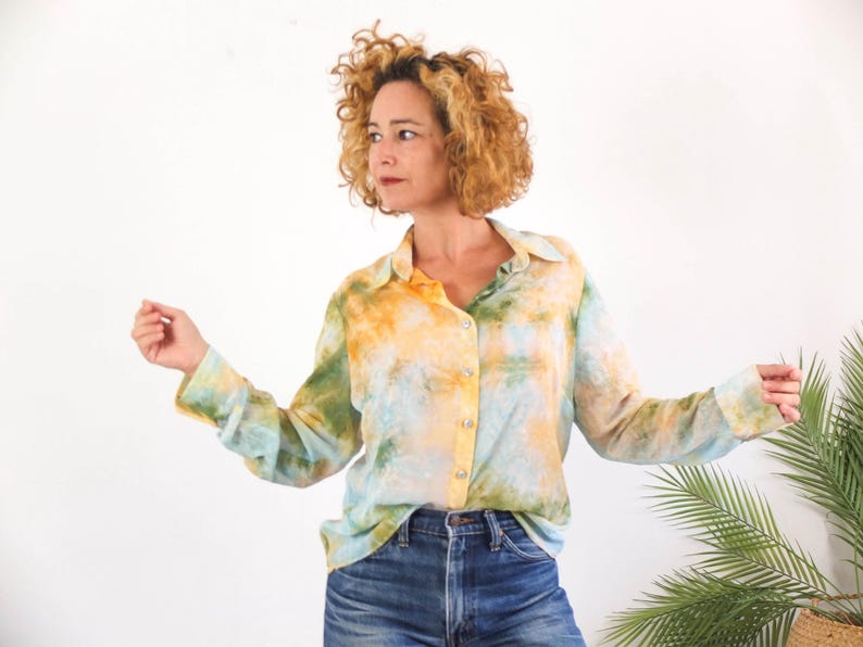 Op de afbeelding: Een overhemd met lange mouwen met een tie-dye patroon in geel, groen en blauw. Het overhemd is geknoopt en wordt gedragen met een blauwe spijkerbroek. Het model staat voor een witte achtergrond.