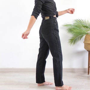 May include: A person wearing black high-waisted jeans with a black shirt tied at the waist.