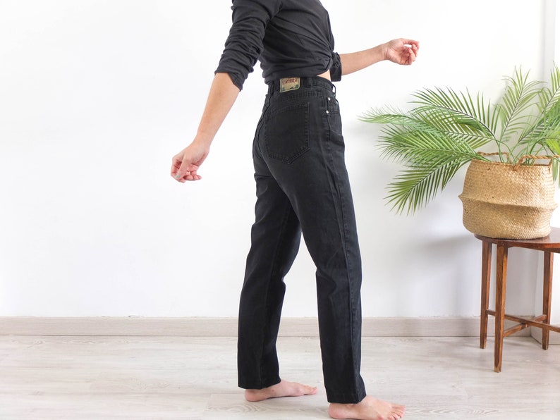 May include: A person wearing black high-waisted jeans with a black shirt tied at the waist.