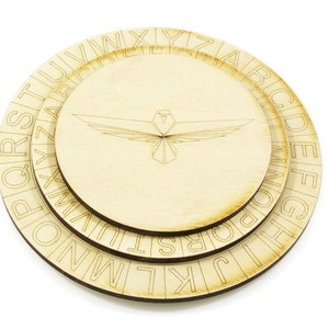 Peut inclure: Trois disques circulaires en bois avec l'alphabet imprimé sur les bords. Les disques sont imbriqués les uns dans les autres, le disque supérieur présentant un motif d'oiseau stylisé.